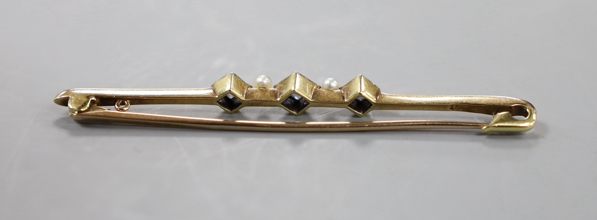 An Edwardian 15ct, three stone sapphire and two stone seed pearl set bar brooch, 57mm, gross 3.4 grams.